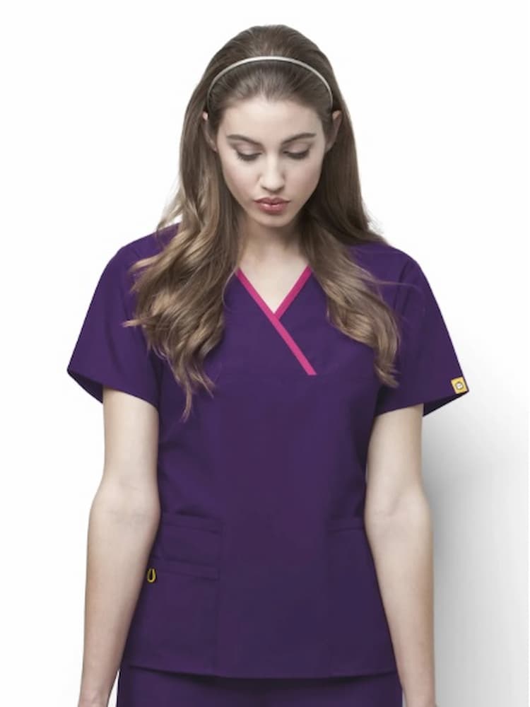A young female Pharmacist wearing a WonderWink Origins Women's Charlie Y-neck Scrub Top in Eggplant size Large featuring a stylish mock wrap neckline & short sleeves.