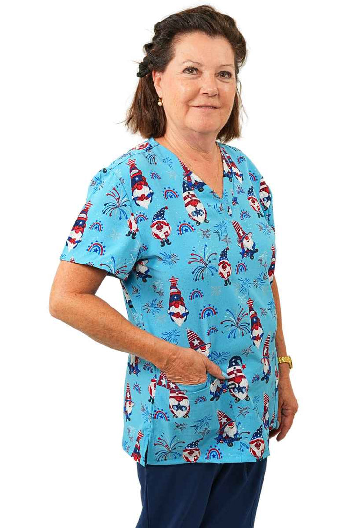 A young female Home Care Health Aide wearing a Luv Scrubs By MedWorks Women's Print Scrub Top in "Star Spangled Gnomes" size Small featuring short sleeves and a classic fit.