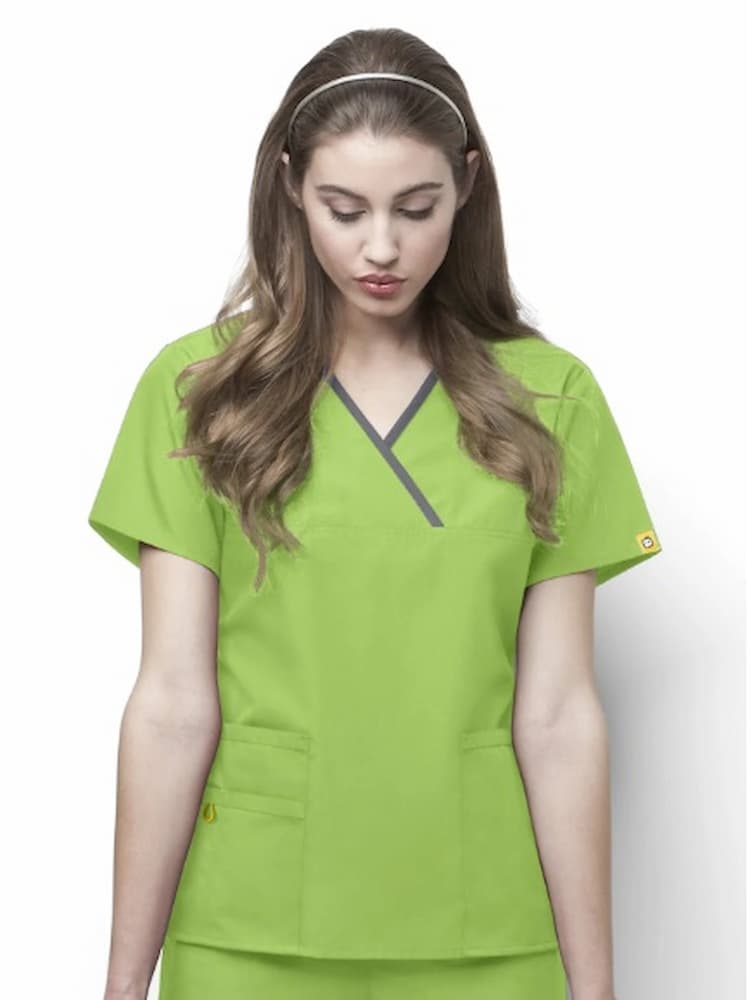 A young female surgeon wearing a WonderWink Origins Women's Charlie Y-neck Scrub Top in Lime Green size Medium featuring a -Neck mock wrap with bungee ID loop at shoulder.