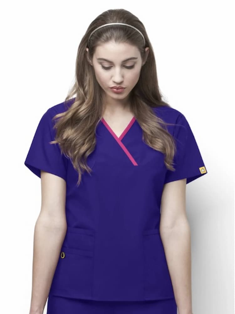 A young female Physical Therapist wearing a WonderWink Origins Women's Charlie Y-neck Scrub Top in Graoe featuring 5 total pockets for all of your on the go storage needs.