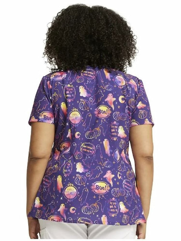 A young female Oncology Nurse wearing a Dickies WOmen's V-Neck Halloween Printed Scrub Top in "Hanging with My Boo" featuring a a center back length of 26".