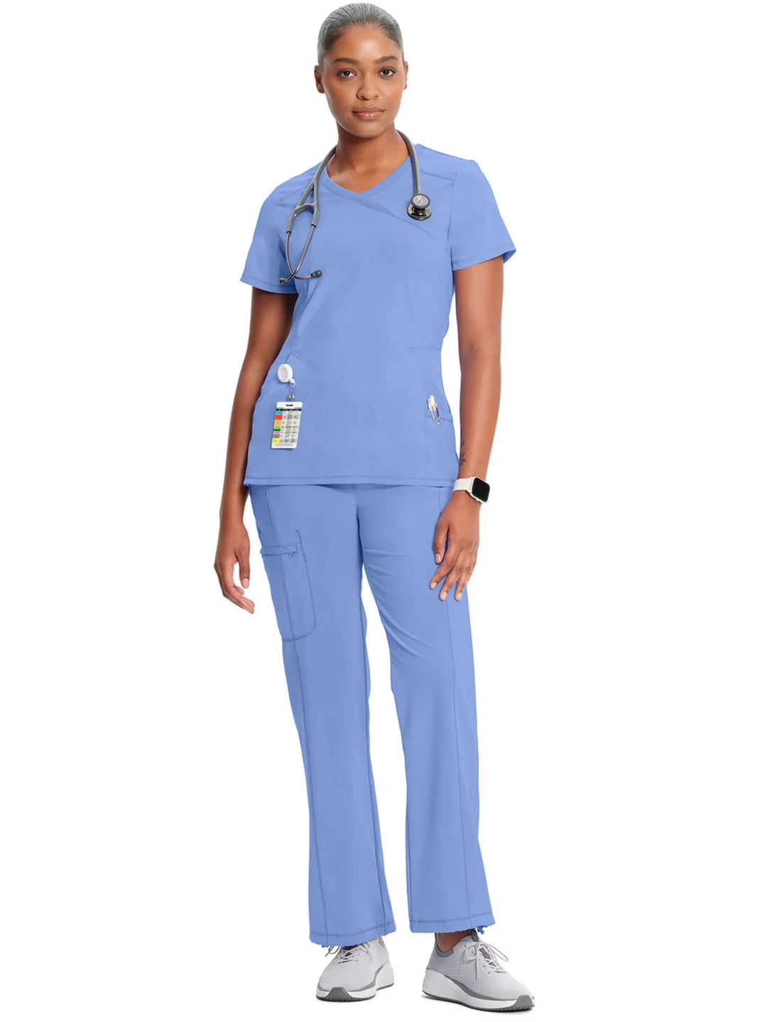 A full body shot of a nurse wearing the Infinity Women's Mock Wrap Scrub Top and Infinity Women's Mid-Rise Scrub Jogger in Ceil Blue on a white background.