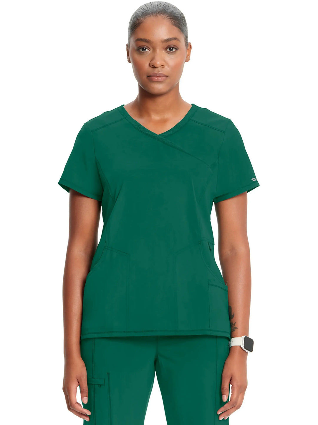 A young female Surgeon displaying the front of the Infinity Women's Mock Wrap Antimicrobial Scrub Top in Hunter Green on a white background.