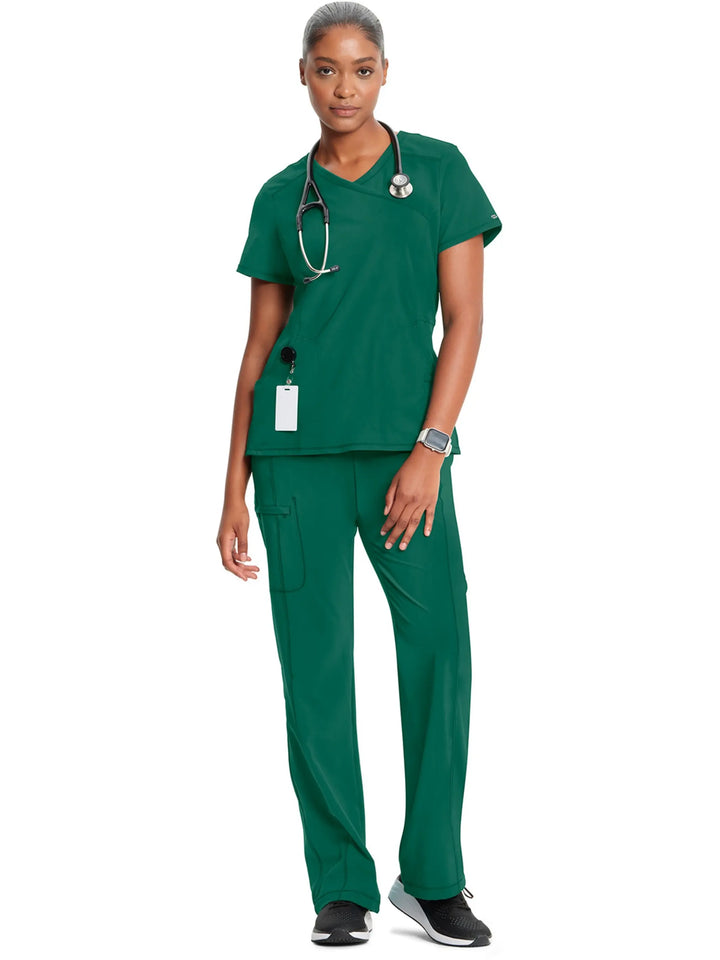 A look at a nurse wearing an Infinity Mock Wrap Scrub Top and an Infinity Women's Mid-Rise Scrub Jogger in Hunter Green on a white background.