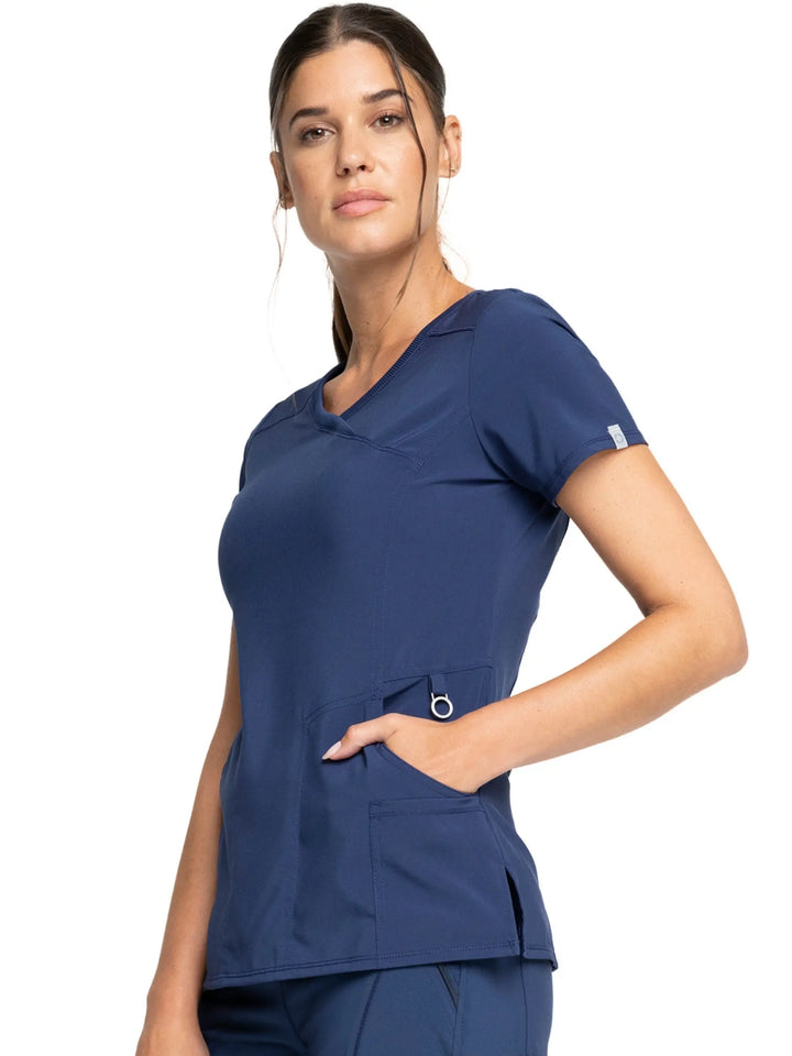 A young female LPN showcasing the left side of the Infinity Women's Mock Wrap Antimicrobial Scrub Top in Navy Blue size Large featuring two pockets on the wearer's left side.