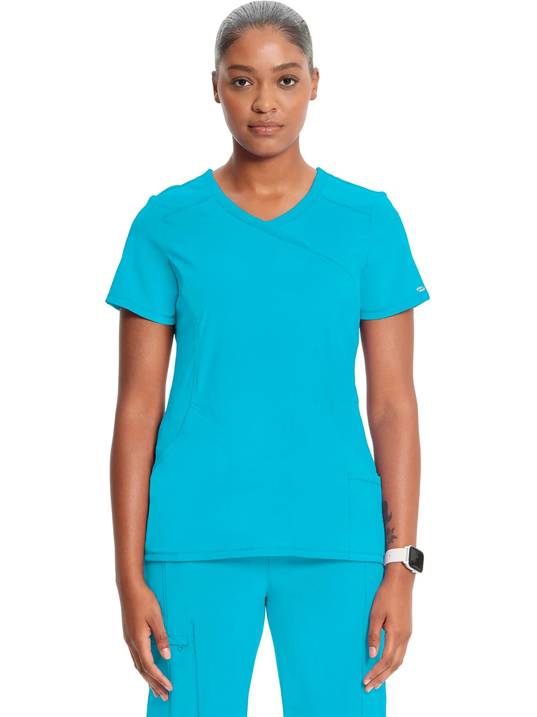 A young female Surgical Assistant displaying the front of the Infinity Women's Mock Wrap Antimicrobial Scrub Top in Turquoise Blue on a white background.