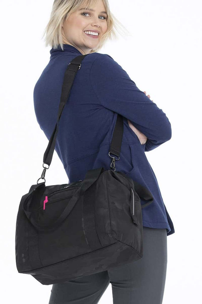 A young female Nurse Practitioner carrying a HeartSoul Madison Duffel Bag in "Black Camo" featuring Heart print polyester lining.