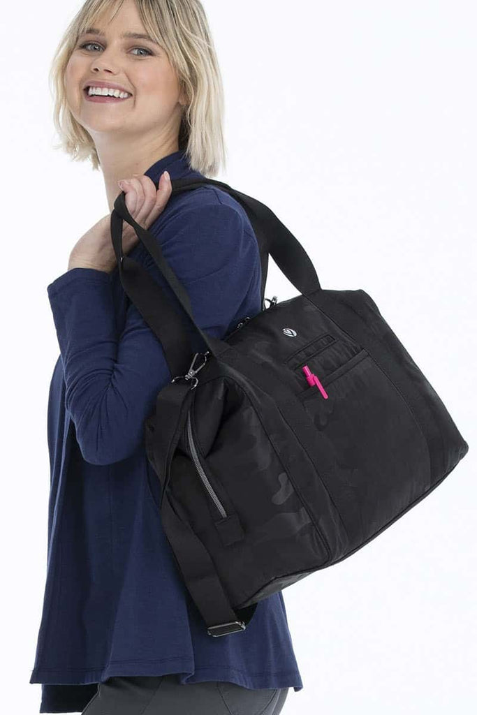 A young female Nurse carrying a HeartSoul Madison Duffel Bag in "Black Camo" featuring large exterior slip pockets on the front and back.