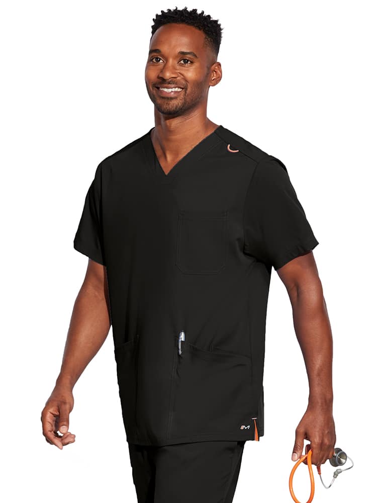 A young male CNA wearing a Barco Motion Unisex V-Neck Scrub Top in Black size Medium featuring a V-neckline with lap over styling.