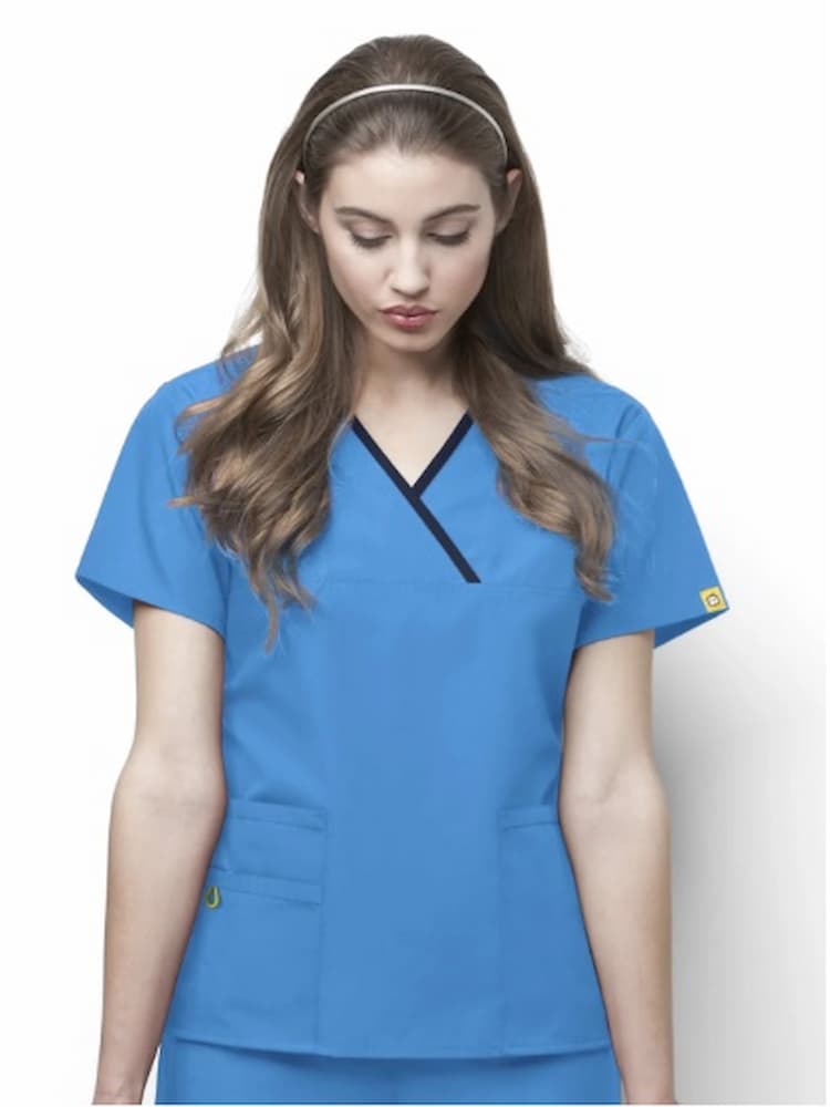 A young female Dental Hygienist wearing a WonderWink Origins Women's Charlie Y-neck Scrub Top in Malibu Blue size Small featuring a "Lady fit". 