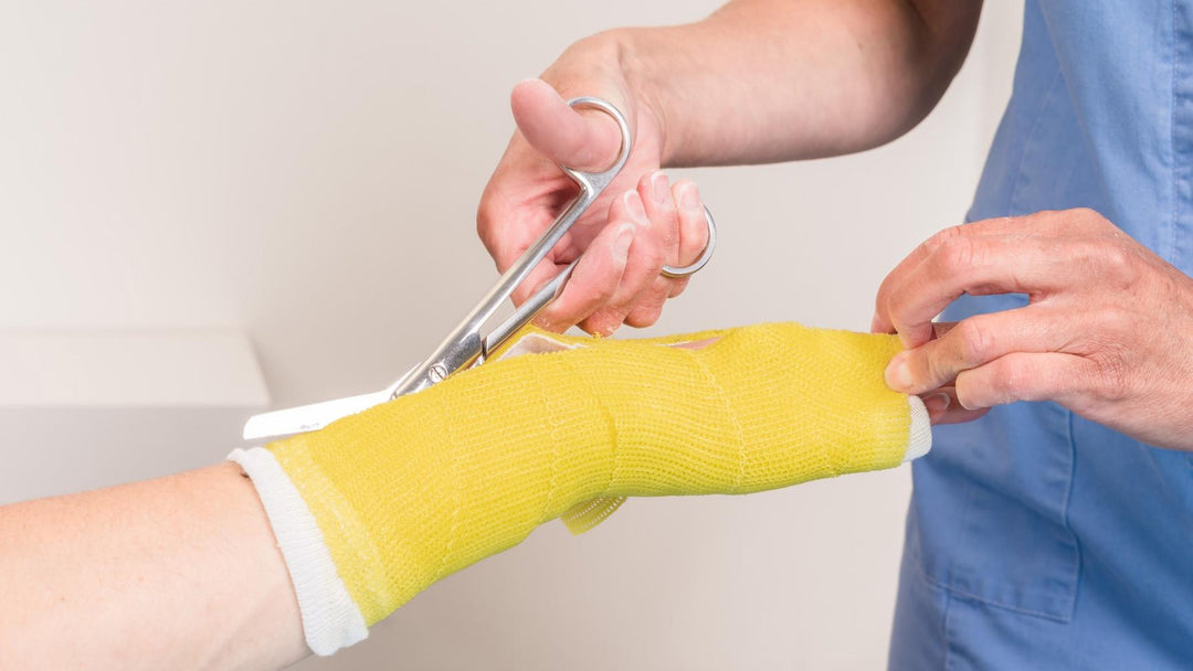 A young female medical assistant using medical scissors from Scrub Pro Uniforms to cut a cast off of a young patient.