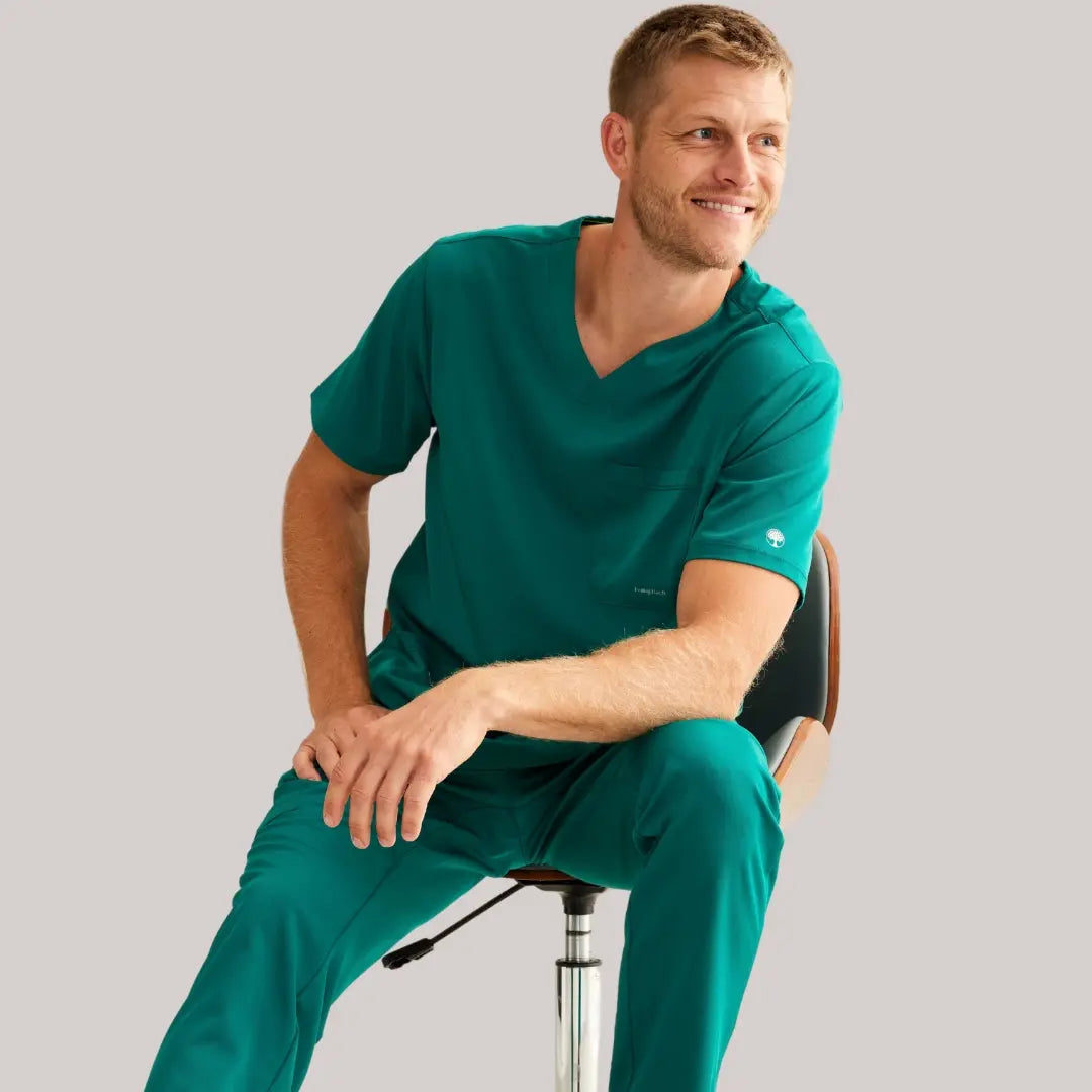 A young male surgical assistant wearing hunter green scrubs from Scrub Pro Uniforms on a light grey background.