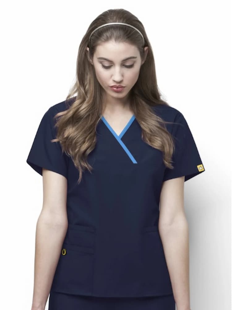 A young female Home Health Aide wearing a WonderWink Origins Women's Charlie Y-neck Scrub Top in Navy size Large featuring 2 lower front patch pockets. 