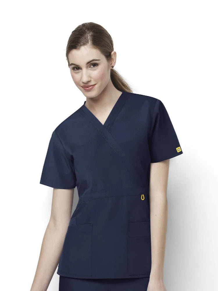 A young female Registered Nurse wearing a WonderWink Origins Women's Fashion Waist Scrub Top in Navy size 2XL featuring a soft poly cotton blended fabric to ensure a comfortable fit all day long.