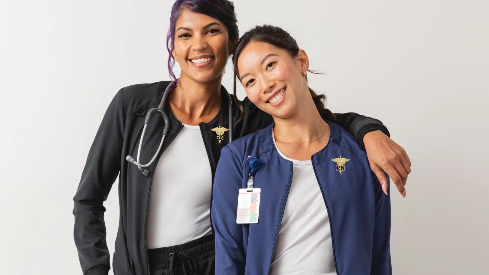 Two young female Registered Nurses showcasing some of the available nurse pins at Scrub Pro.