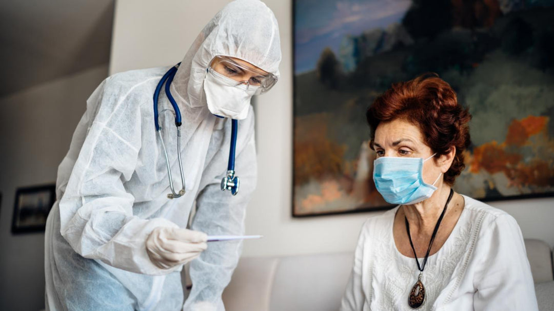 A young medical professional covered in Personal Protective Equipment from Scrub Pro Uniforms tending to an elderly patient.