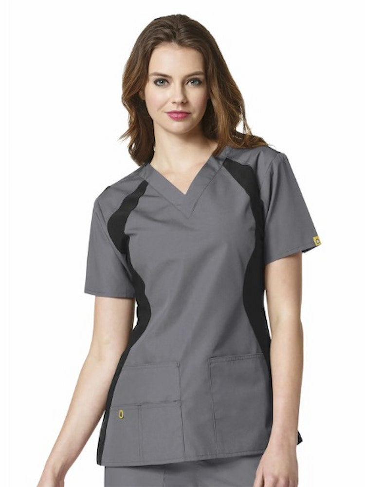 A young female LPN wearing a WonderWink Origins Women's Lima Knit Panel Scrub Top in Pewter size Medium featuring a total of 5 pockets.
