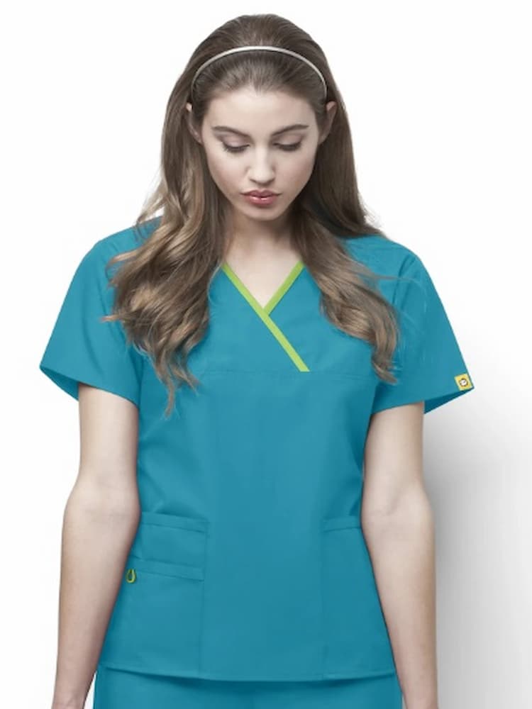 A young female Surgeon's Assistant wearing a WonderWink Origins Women's Charlie Y-neck Scrub Top in Real Teal in size Medium featuring 5 total pockets.