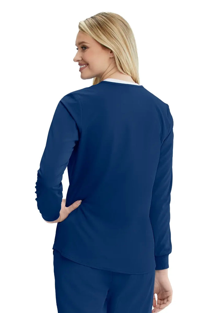 A young female Diagnostic Medical Sonographer showcasing the back of the Skechers Women's Stability Snap Front Scrub Jacket in Navy size Large featuring a curved hemline.