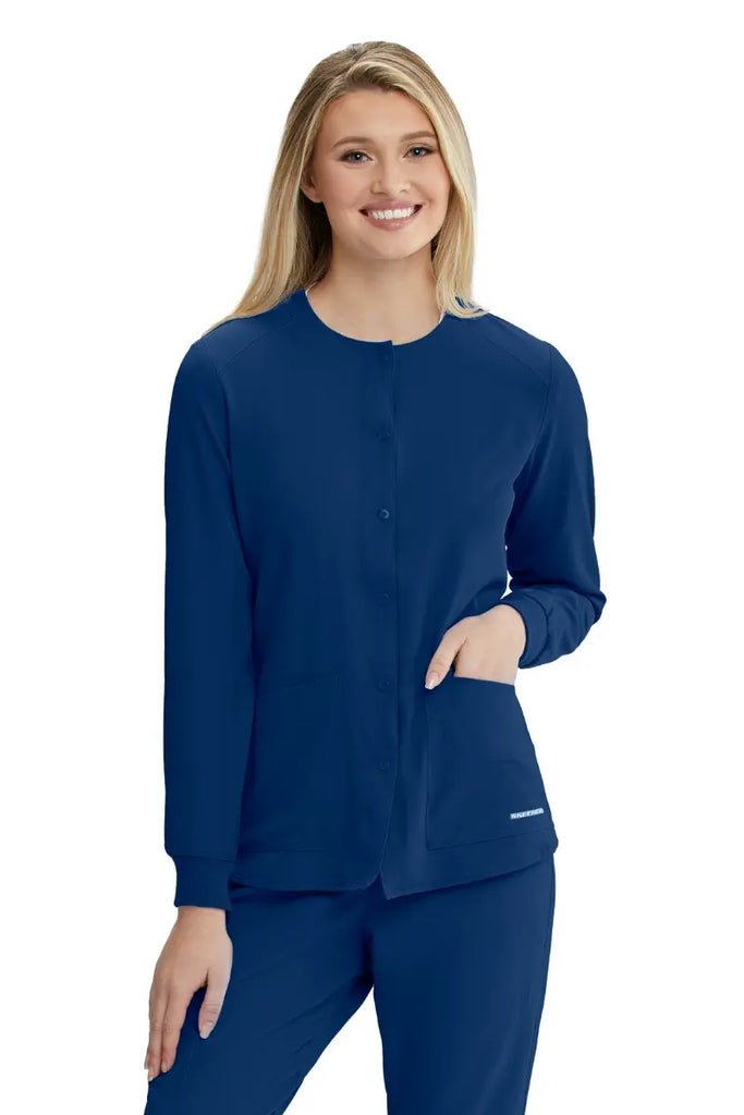 A young female LPN wearing a Skechers Women's Stability Snap Front Scrub Jacket from Skechers in Navy featuring a junior contoured fit with a round neckline.