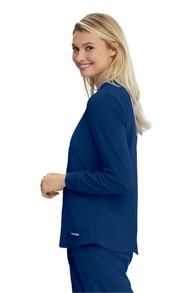 A young female Medical Assistant showcasing the Skechers Women's Stability Snap Front Scrub Jacket in Navy size Medium featuring long sleeves with rib knit cuffs.