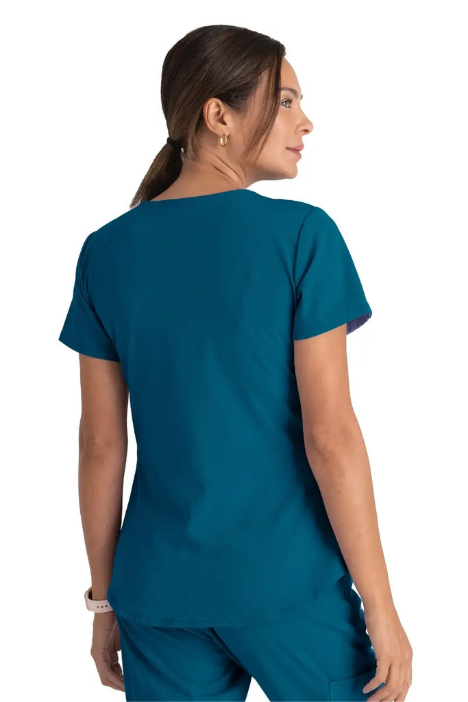 A young female Nurse wearing a Skechers Women's Breeze V-neck Scrub Top in Bahama size Medium featuring a center back length of 25.5".