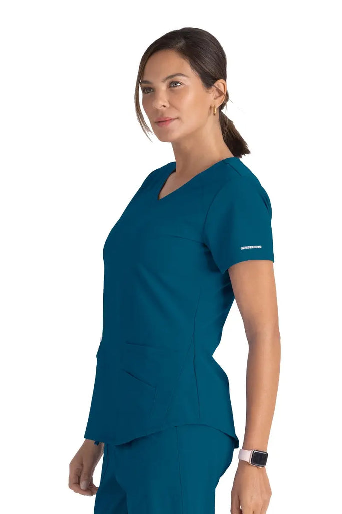 A young female CNS wearing a Skechers Women's Breeze V-neck Scrub Top in Bahama size XL featuring the Skechers logo at the left sleeve.