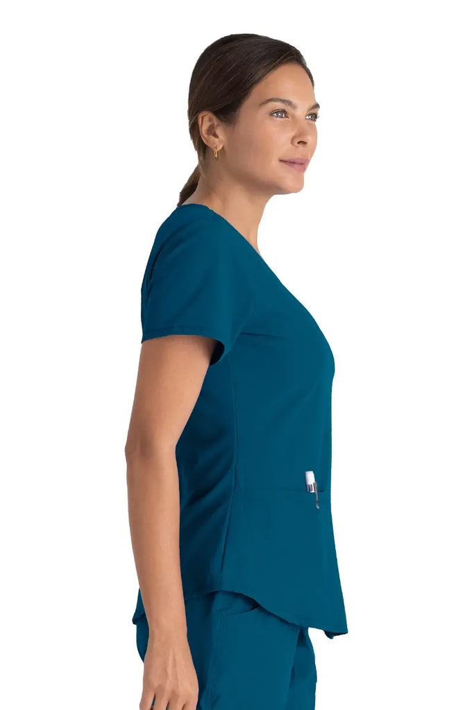 A young female Nurse Practitioner wearing a Skechers Women's Breeze V-neck Scrub Top in Bahama size XL featuring a shaped hem.