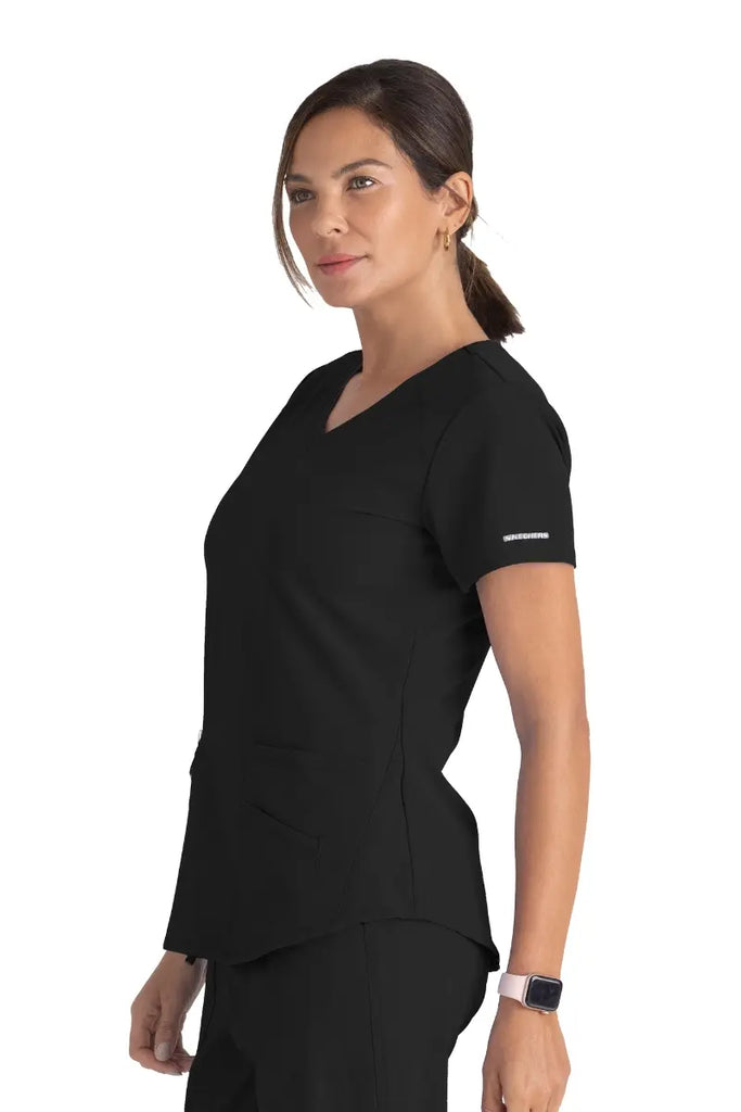 A young female Surgeon wearing a Skechers Women's Breeze V-neck Scrub Top in Black size Medium featuring a center back length of 25.5".