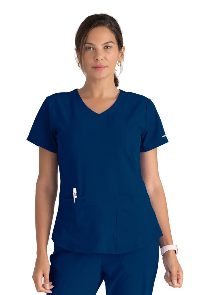 A young female CNA wearing a Women's Breeze V-neck Scrub Top from Skechers in Navy featuring short sleeves.