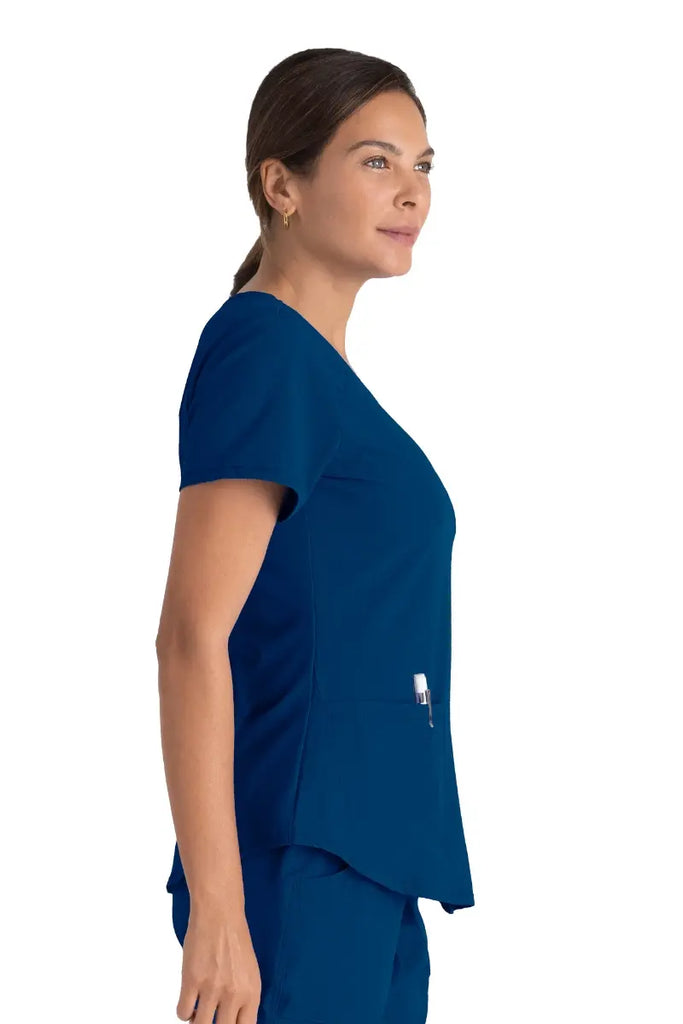 A young female Certified Nursing Assistant wearing a Skechers Women's Breeze V-neck Scrub Top in Navy featuring a curved hemline.