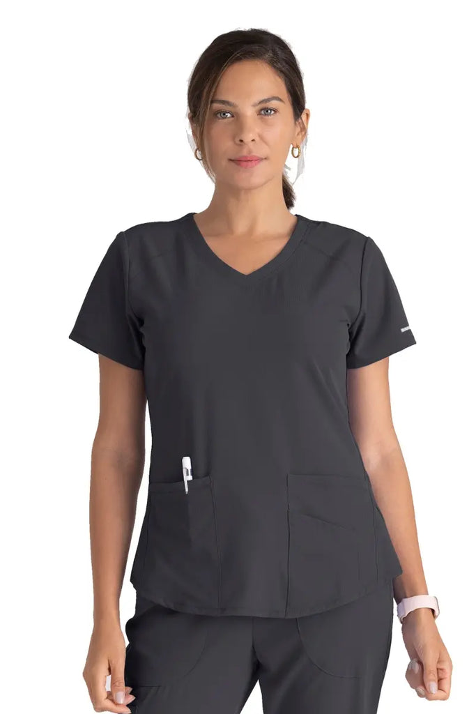 A young female CNA wearing a Women's Breeze V-neck Scrub Top from Skechers in Pewter featuring contrast bending detail at the neckline.