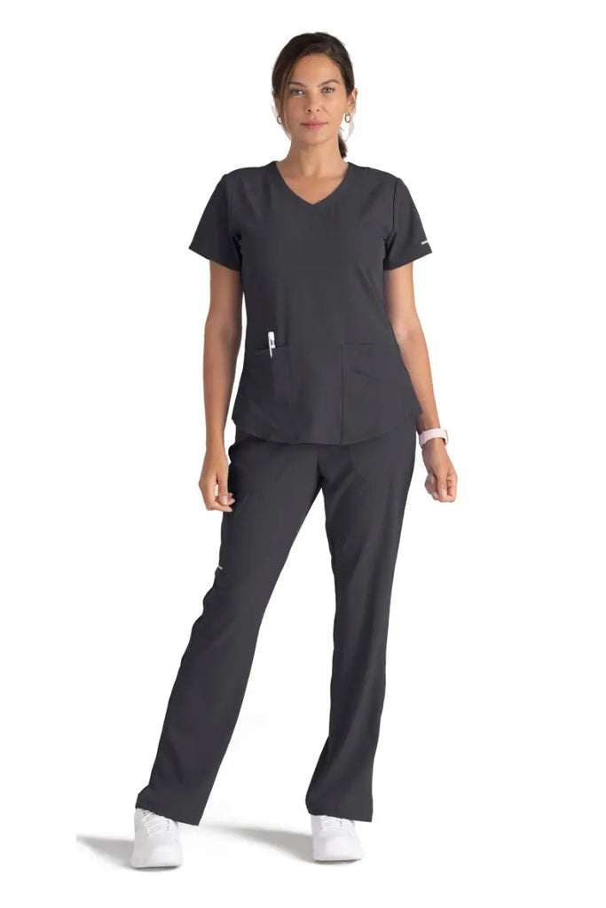 A full body shot of a young female Phlebotomist wearing a Skechers Women's Breeze V-neck Scrub Top in Pewter size Large featuring two front patch pockets and a utility pocket for all storage needs.