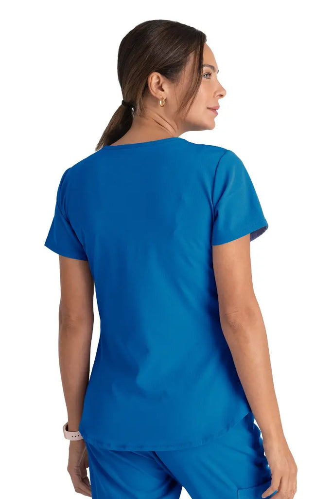 A young female Surgeon wearing a Skechers Women's Breeze V-neck Scrub Top in Royal size Medium featuring a center back length of 25.5".