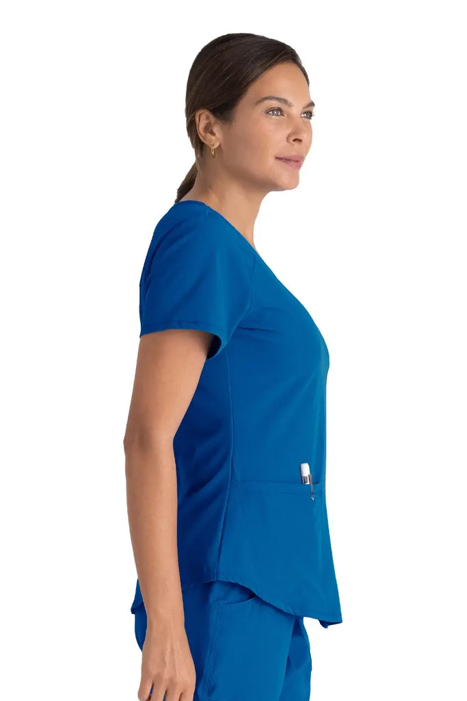 A young female Doctor wearing a Doctor wearing a Skechers Women's Breeze V-neck Scrub Top in Royal size Small featuring a shaped hem.