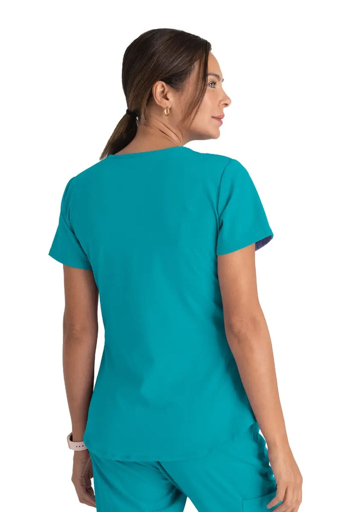 A young female Surgical Assistant wearing a Skechers Women's Breeze V-neck Scrub Top in Teal size Medium featuring a center back length of 25.5".
