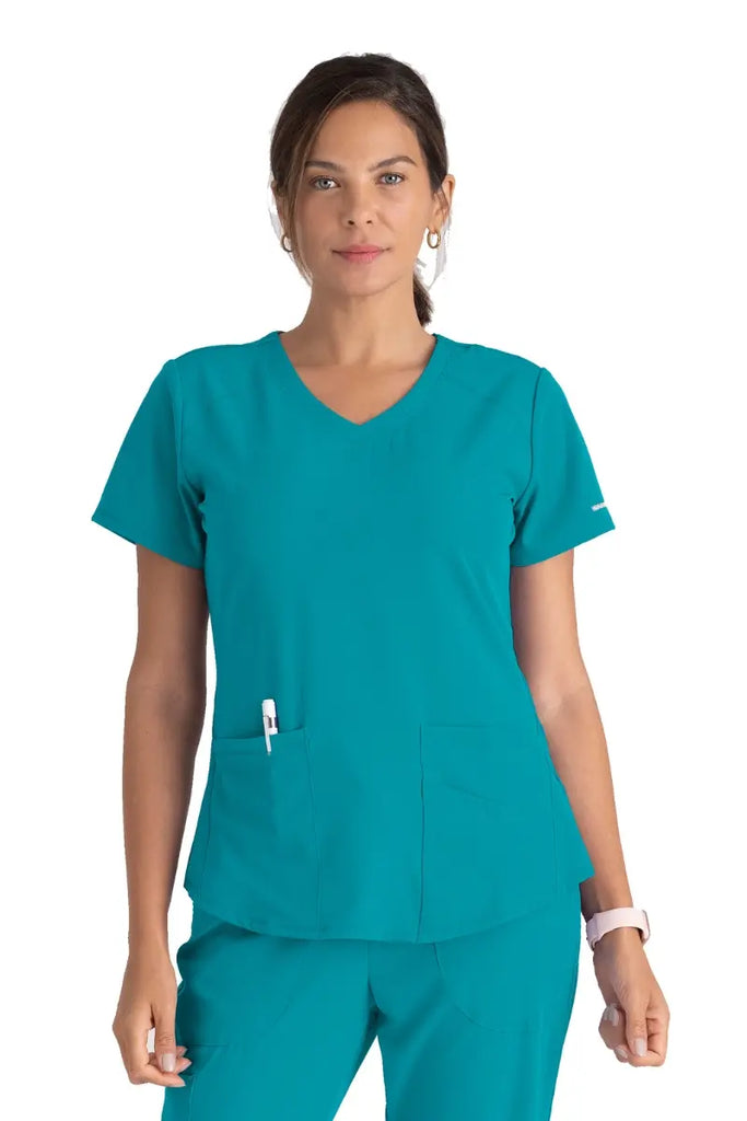 A young female CNA wearing a Women's Breeze V-neck Scrub Top from Skechers in Teal featuring a modern fit.