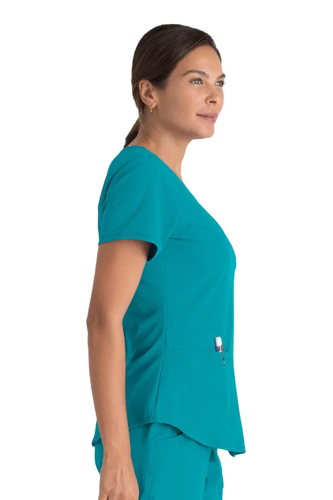 A young female LVN wearing a Skechers Women's Breeze V-neck Scrub Top in Teal size Large featuring a shaped hemline.