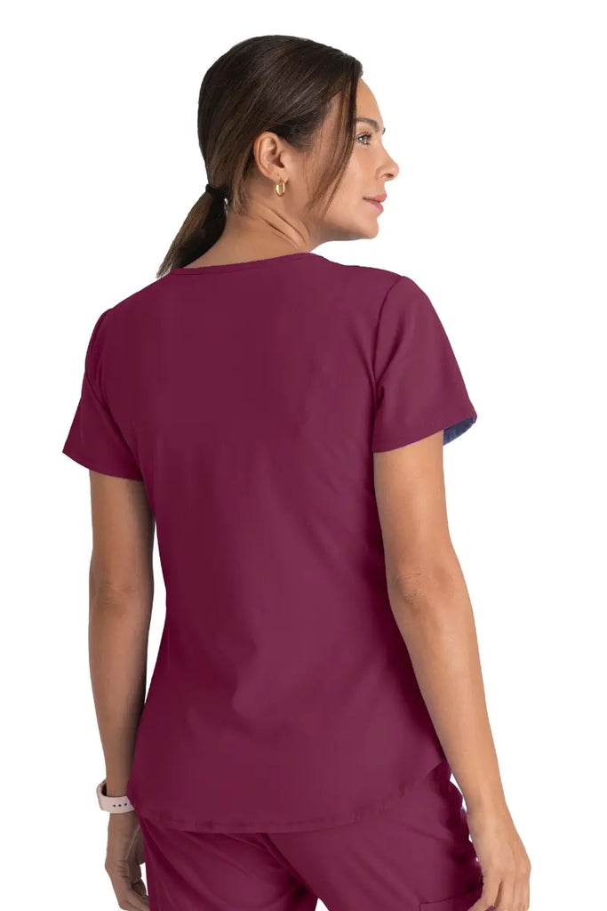 The back of a young female LPN wearing a Skechers Women's Breeze V-neck Scrub Top in Wine size Medium featuring a center back length of 25.5".
