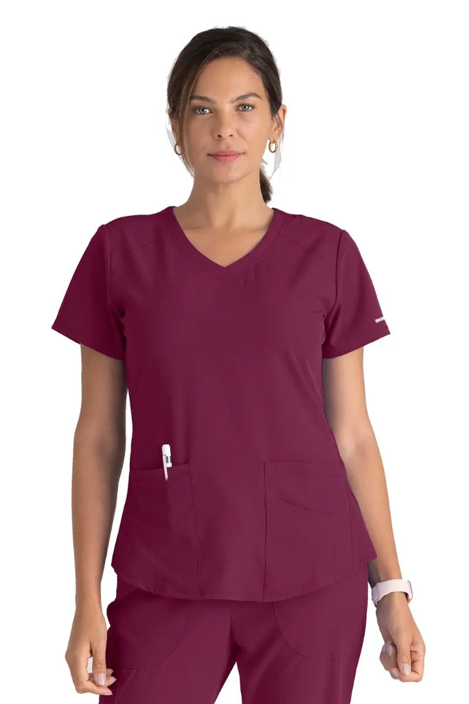 A young female CNA wearing a Women's Breeze V-neck Scrub Top from Skechers in Wine featuring a modern fit.