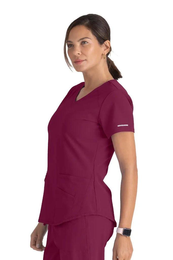 A young female Nurse wearing Skechers Women's Breeze V-neck Scrub Top in Wine size XL featuring a shaped hem.