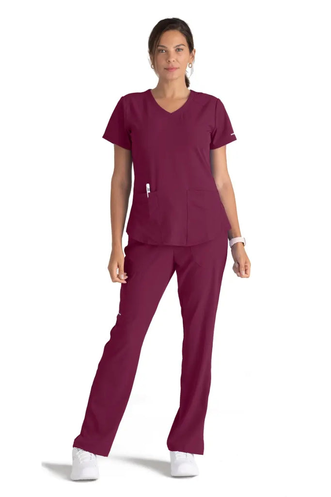 A young female Cardiovascular Nurse wearing a Skechers Women's Breeze V-neck Scrub Top in Wine size Large featuring two front patch pockets.