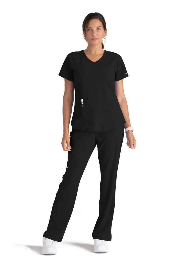 A full body shot of a young female EMT wearing a black Skechers scrub uniform on a white background.