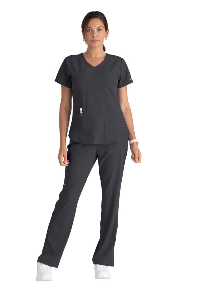 A full body shot of a young female Pharmacy Tech wearing a Pewter scrub uniform from Skechers.