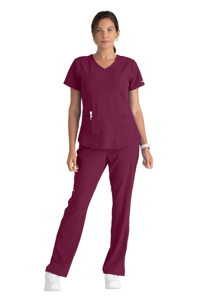 A full body shot of a young female Cardiovascular Nurse wearing a Skechers Women's Scrub Uniform in Wine.
