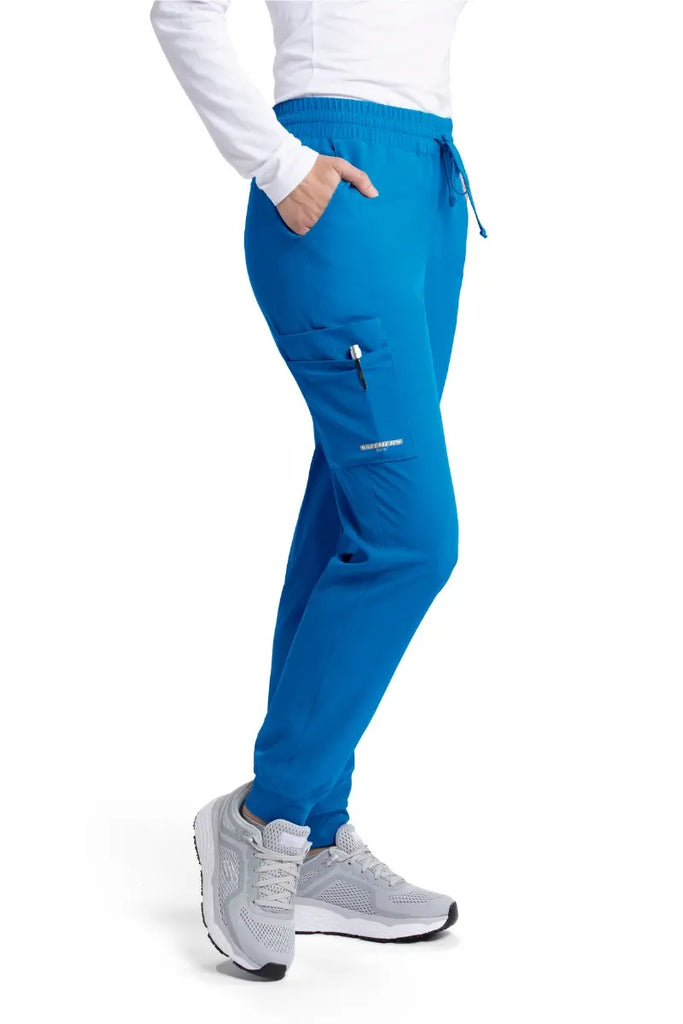 The right side of the Skechers Women's Theory Scrub Joggers in New Royal featuring an exterior cargo pocket with the Skechers logo printed on it located on the right side leg.