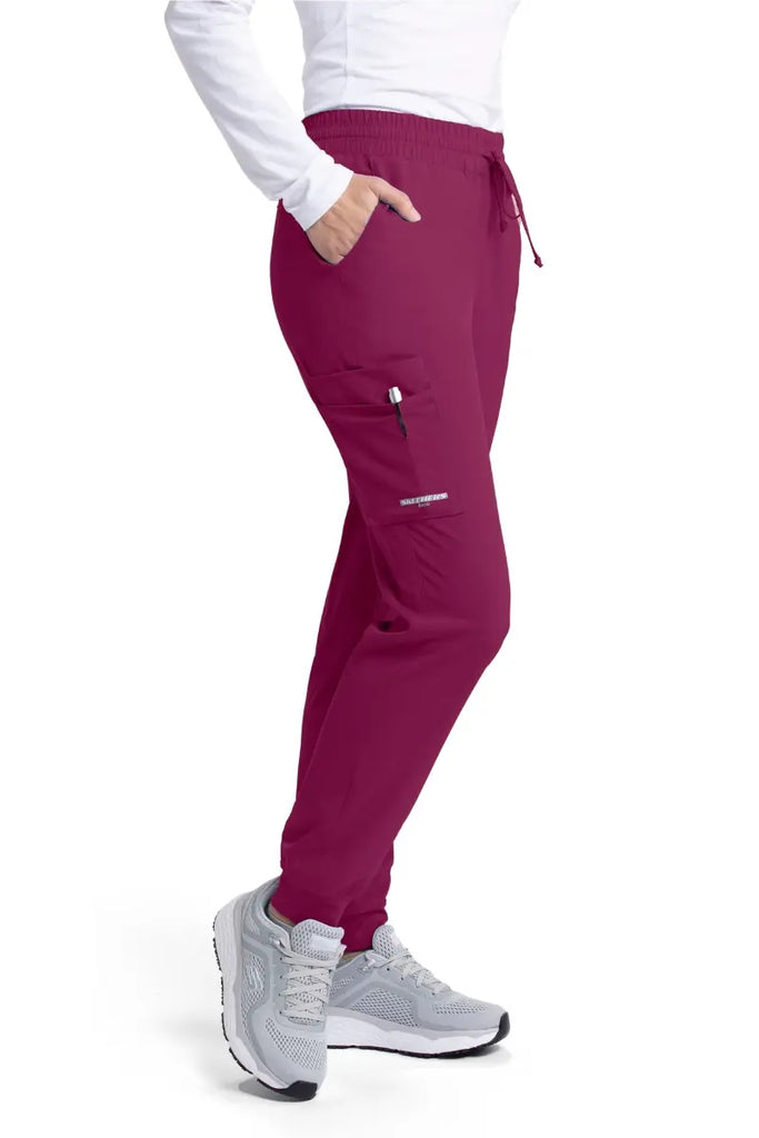 The right side of the Skechers Women's theory Jogger Scrub Pants in Wine size Small featuring two front slanted pockets and an outside cargo pocket..