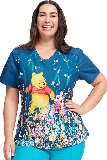 A young female nurse wearing a Women's V-Neck Print Top from Cherokee Tooniforms in "Flower Walk" featuring a rounded V-neckline with contrast piping.