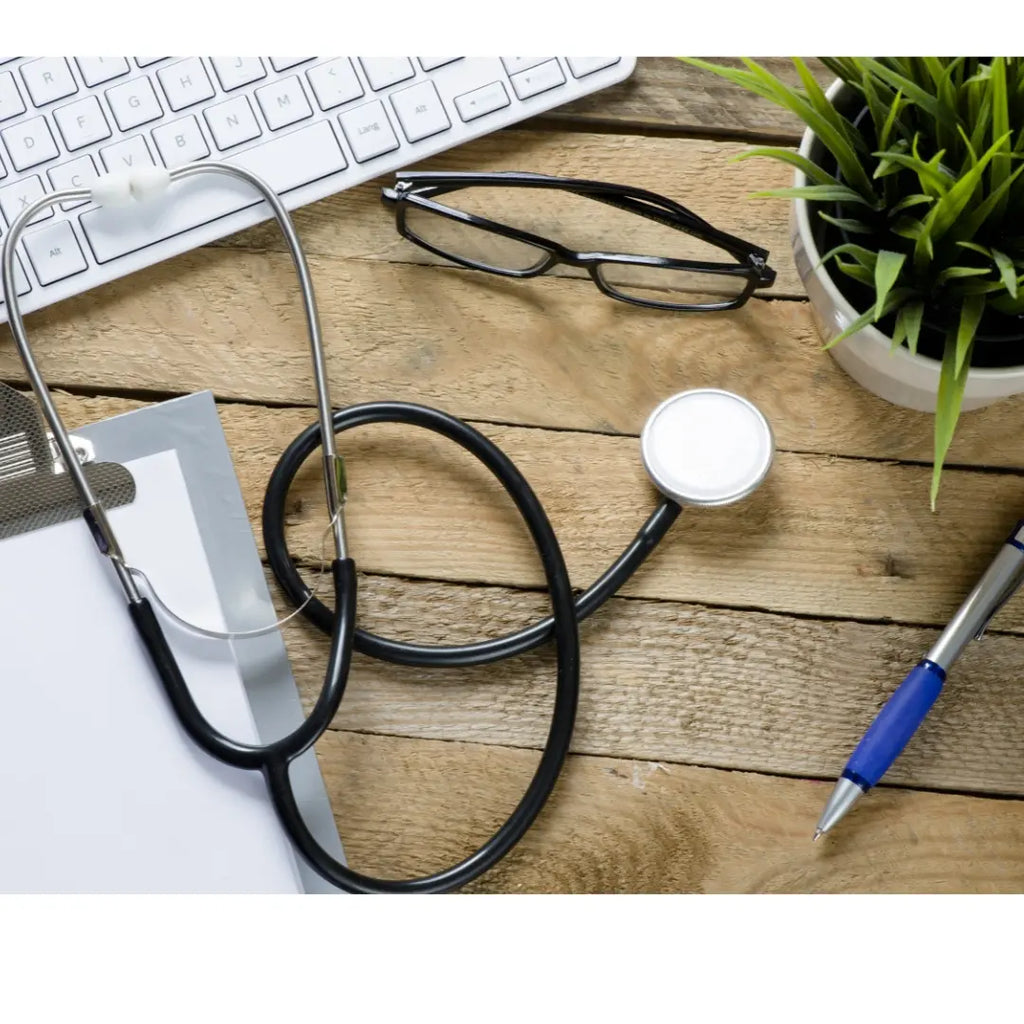 Desktop showing a laptop, stethoscope, clipboard, glasses, plant, and pen.