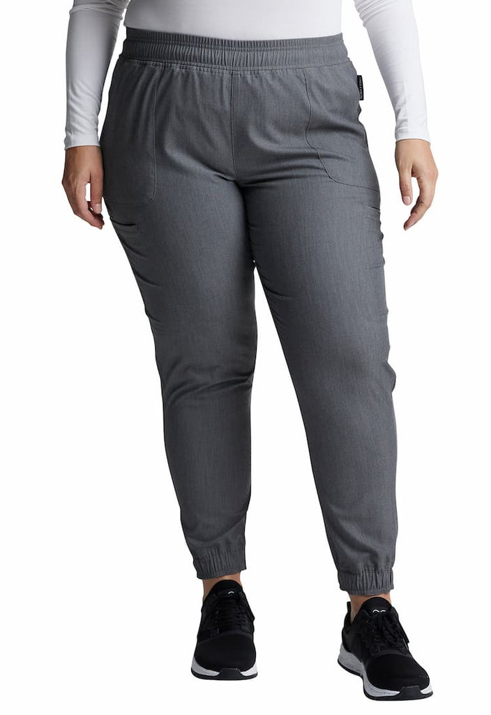 A young female Medical Assistant wearing a pair of Vince Camuto Women's Mid Rise Scrub Joggers in Heathered Charcoal size 3XL featuring an elastic-reinforced drawstring to ensure a comfortable all day fit.